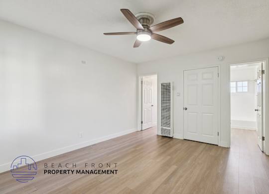 A room with a ceiling fan and wooden floors, with a logo for Beach Front Property Management in the bottom left corner.