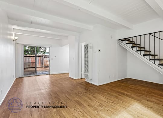 A spacious room with wooden floors and a staircase with a metal railing.