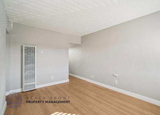 A spacious room with a wooden floor and a window with blinds.