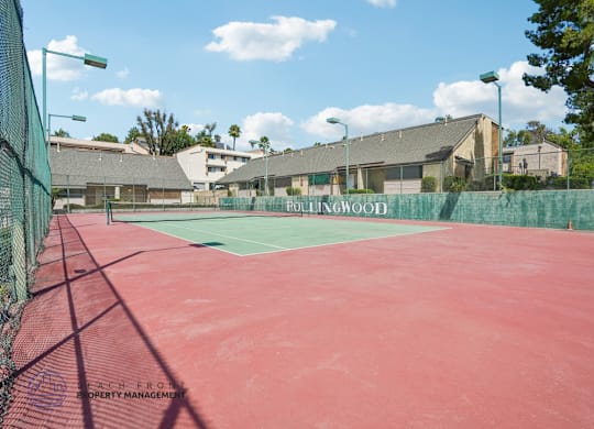A red tennis court with a green fence and the words