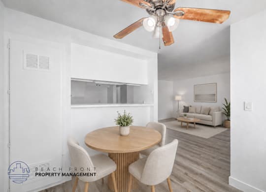 A dining room with a round table and chairs, a ceiling fan, and a living room with a couch in the background.