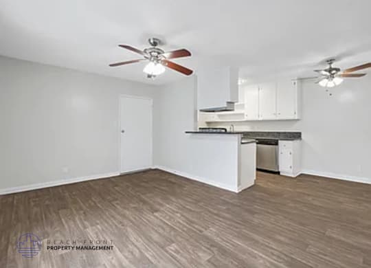 A spacious room with a kitchenette and two ceiling fans.