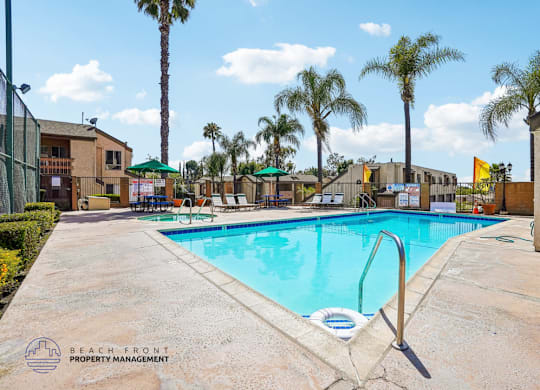 A pool surrounded by palm trees and a building in the background.