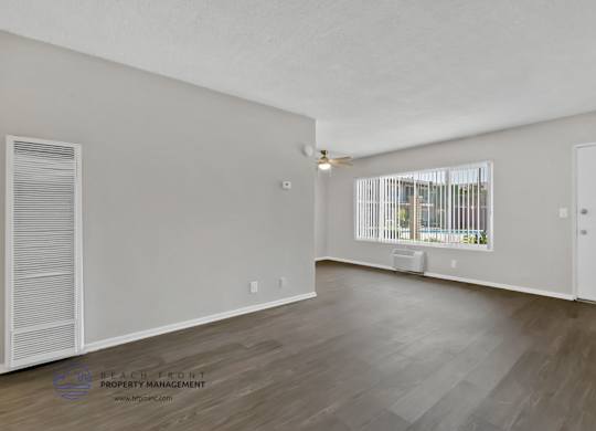 A spacious room with wooden flooring and a window with blinds.