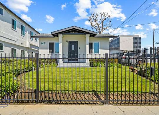 the front of a house with a yard behind a fence
