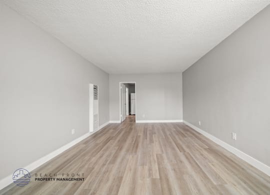 A spacious room with wooden flooring and white walls, with a doorway leading to another room.