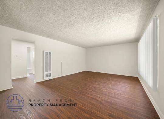 A room with wooden floors and white walls, with a logo for Beach Front Property Management in the bottom left corner.