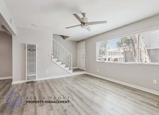 A spacious room with a ceiling fan and a staircase leading to another floor.