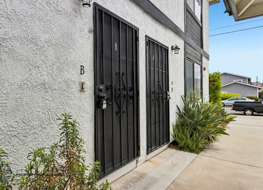 A black gate with the letter B above it is on a white wall.