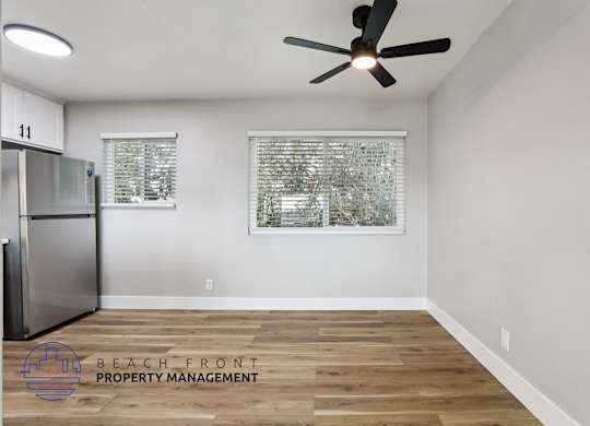 A room with a ceiling fan and a fridge in it.