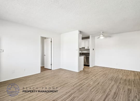 A room with wooden flooring and white walls, with a logo for Beach Front Property Management in the bottom left corner.
