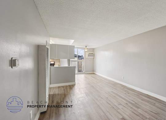 A spacious room with wooden flooring and a logo for Beach Front Property Management in the corner.