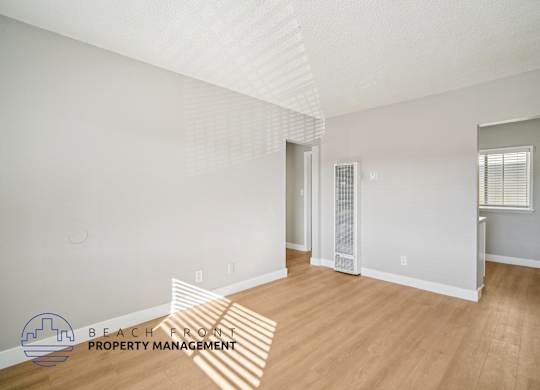 A room with wooden floors and white walls, with a window on the right wall.