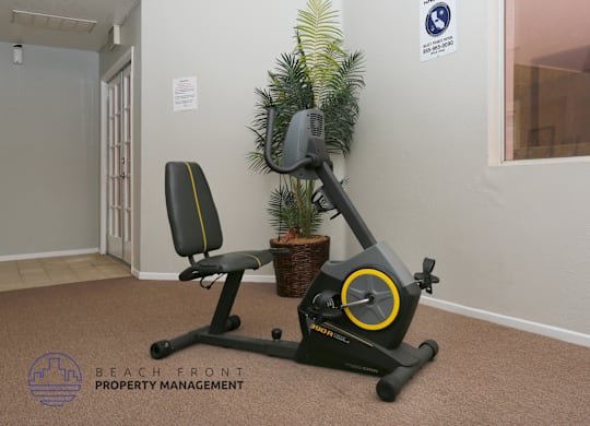 A stationary exercise bike is placed in a room with a potted plant and a sign on the wall.