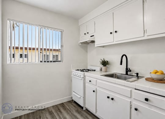 A kitchen with white cabinets and a window with blinds.
