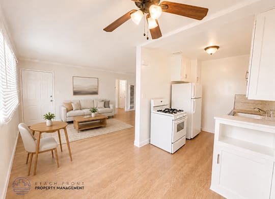 A living room with a dining table and chairs, a kitchen with a refrigerator, stove, and sink, and a ceiling fan.