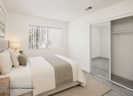A bedroom with a bed, a window with blinds, a rug, and a mirror.
