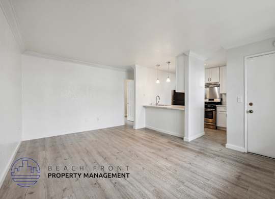 A spacious room with wooden flooring and a kitchen area in the background.