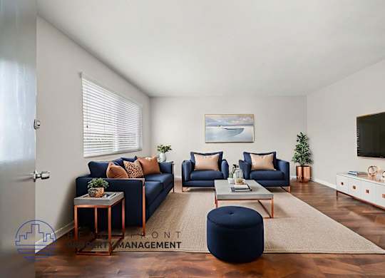 A living room with a blue ottoman and a television on the wall.