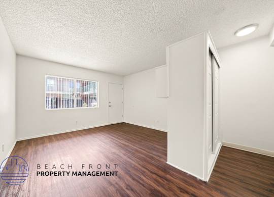 A room with wooden floors and white walls, with a window showing a view of a building.