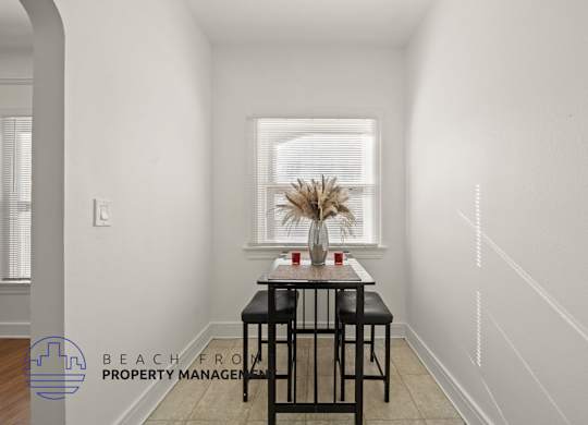 A dining table with two chairs is in a white room with a window.
