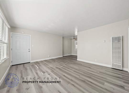 A spacious room with wooden flooring and a logo for Beach Front Property Management.