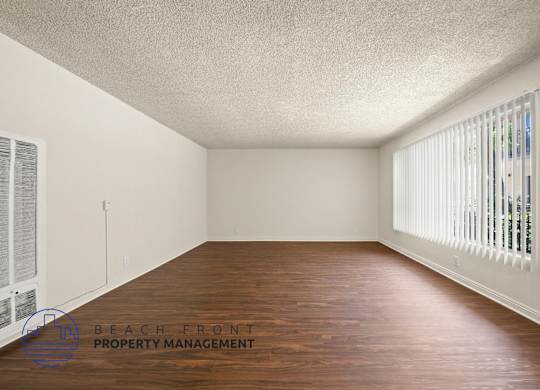 A room with wooden floors and white walls, with a window on the right side.