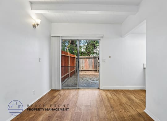 A room with a wooden floor and a sliding glass door leading to a backyard.
