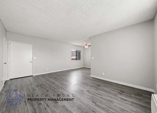 A spacious room with wooden flooring and a logo for Beach Front Property Management in the corner.