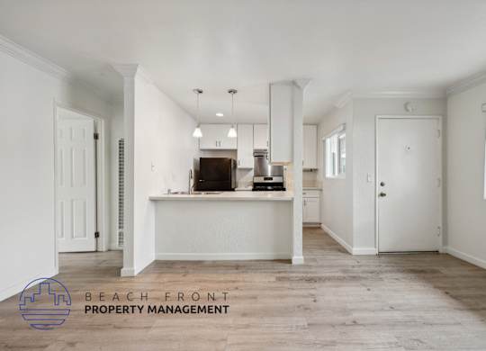 A spacious, empty room with a kitchenette and a logo for Beach Front Property Management.