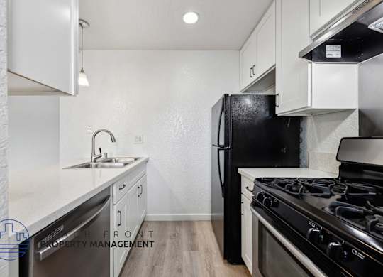 A kitchen with a black fridge and stove top oven.