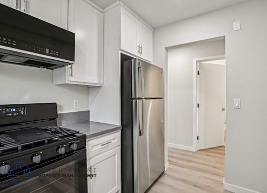 A modern kitchen with a stove top oven, refrigerator, and cabinets.