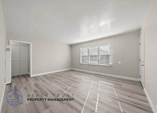 A spacious room with wooden flooring and a window with blinds.