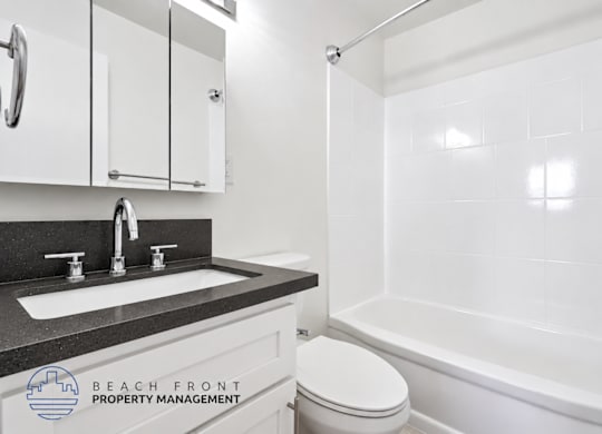 A white bathroom with a black countertop and a shower with a glass door.