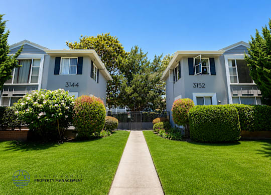 Two identical houses are located next to each other with a concrete pathway in between.