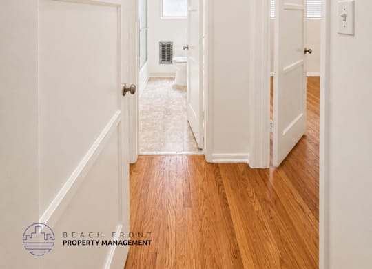A hallway with white walls and wooden floors leading to a balcony.