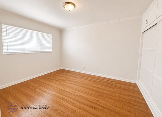 A room with wooden flooring and white walls, with a window on the left side.