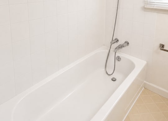 A white bathtub with a shower head and a window with blinds.