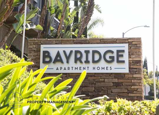 A sign for Bayridge Apartment Homes is displayed in front of some greenery.