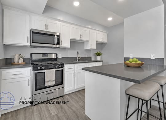 A modern kitchen with a stove, oven, microwave, and bar stools.