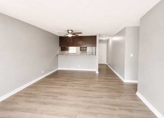 A spacious room with a ceiling fan and a kitchenette in the background.