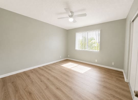 A room with a ceiling fan and a window with blinds.
