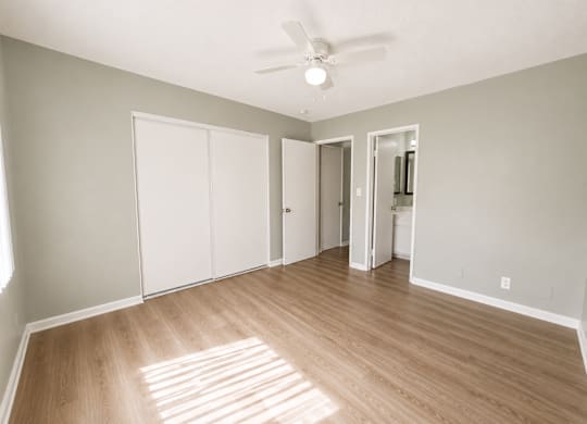 A room with a ceiling fan and light, hardwood floors, and white walls with a doorway leading to another room.