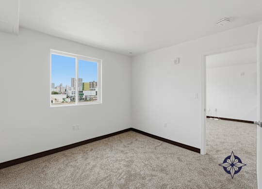 A room with a carpeted floor and a window showing a cityscape outside.