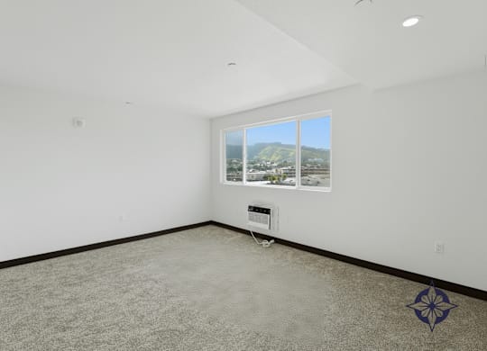 A room with a carpeted floor and a window overlooking a cityscape.