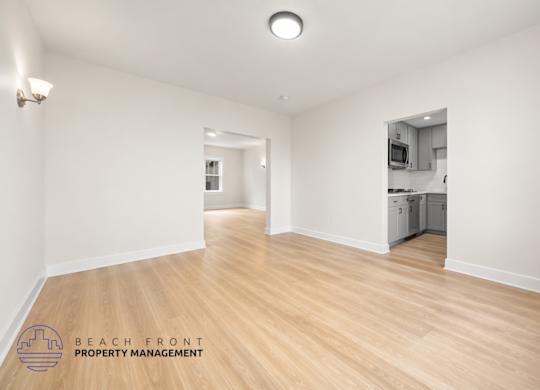 A spacious room with wooden floors and a logo for Beach Front Property Management in the bottom left corner.