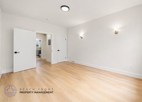 A spacious room with wooden floors and white walls, managed by Beach Front Property Management.