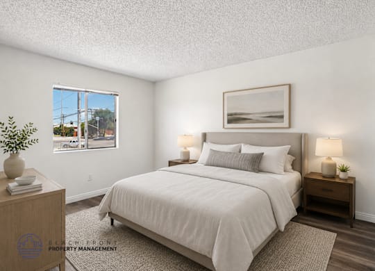 A well-lit bedroom with a large bed, a nightstand with a lamp, and a framed picture on the wall.
