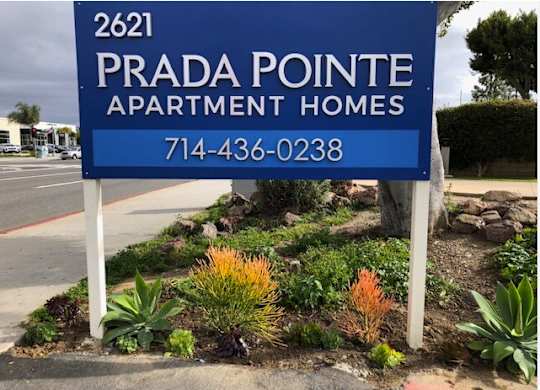 A blue sign for Prada Pointe Apartment Homes with a phone number on it.