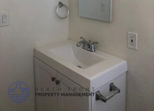 A bathroom with a sink, mirror and a logo for Beach Front Property Management.